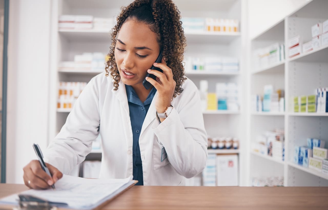 Phone call, pharmacist woman and writing on medicine checklist, customer service or virtual pharmacy support. Serious doctor with medical notes, health insurance documents and talking at help desk.